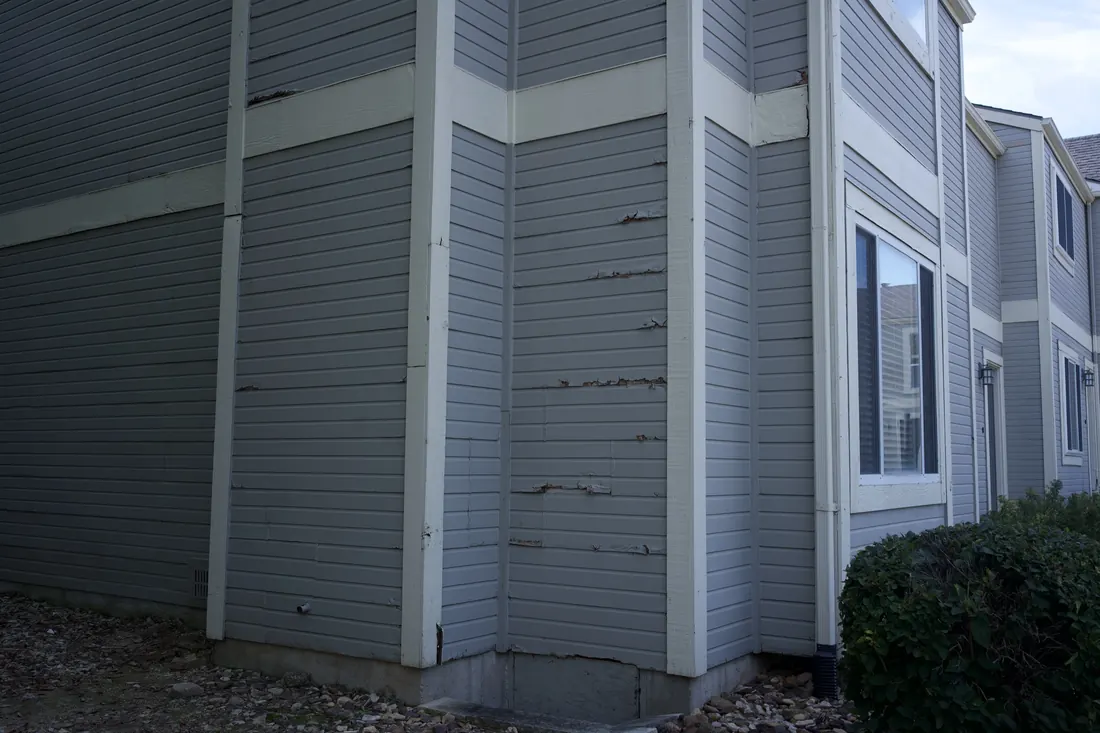 Cracked and splitting lap siding at the corner of an apartment block
