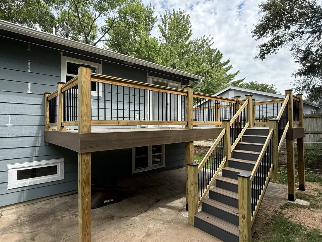 Elevated deck, black balusters and stairs seen from the side of the yard