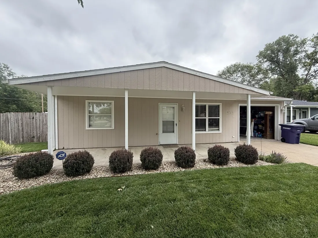 Covered front porch with plain white posts and streaked vertical siding before the recladding