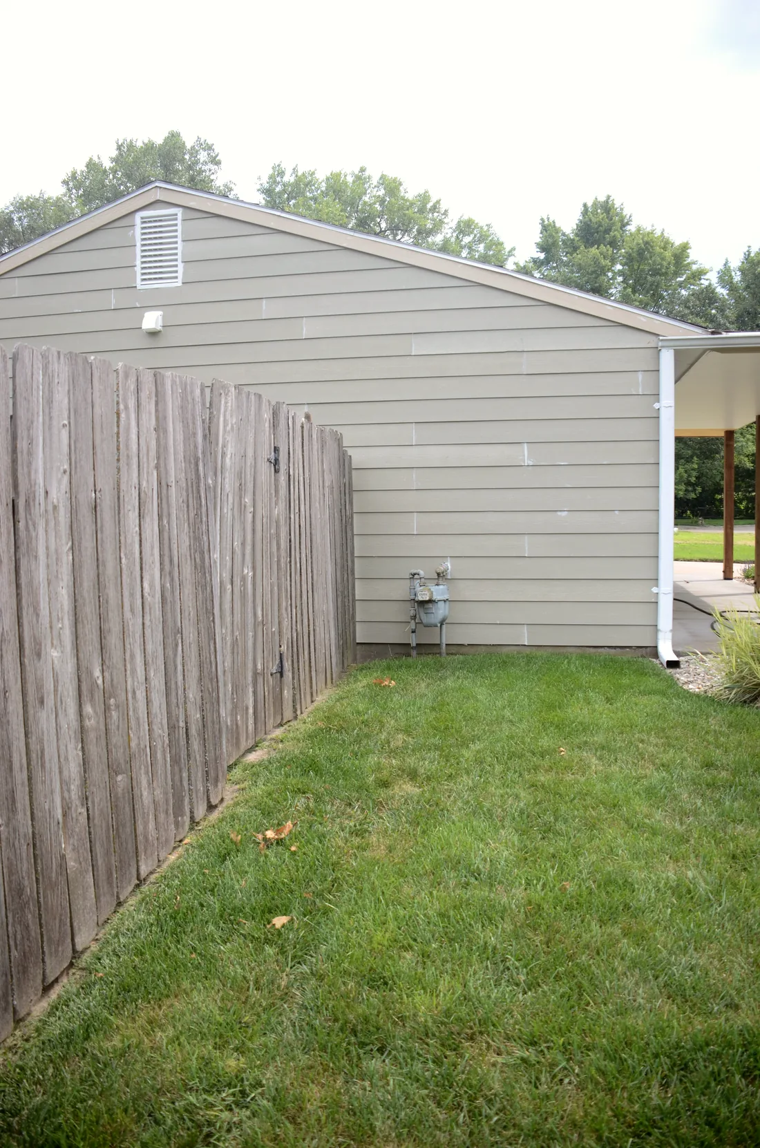 New siding, gutter and downspout running down the side of a house to the fence line