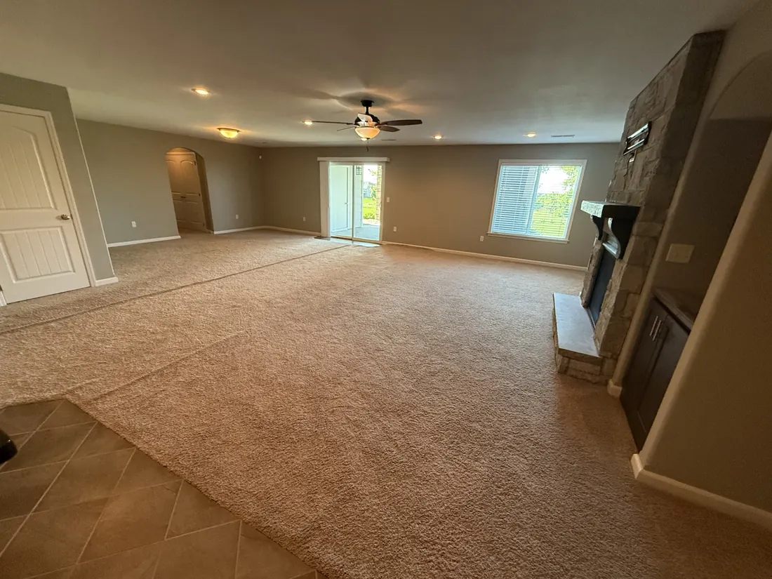Open great room carpeted wall to wall beside a stone hearth