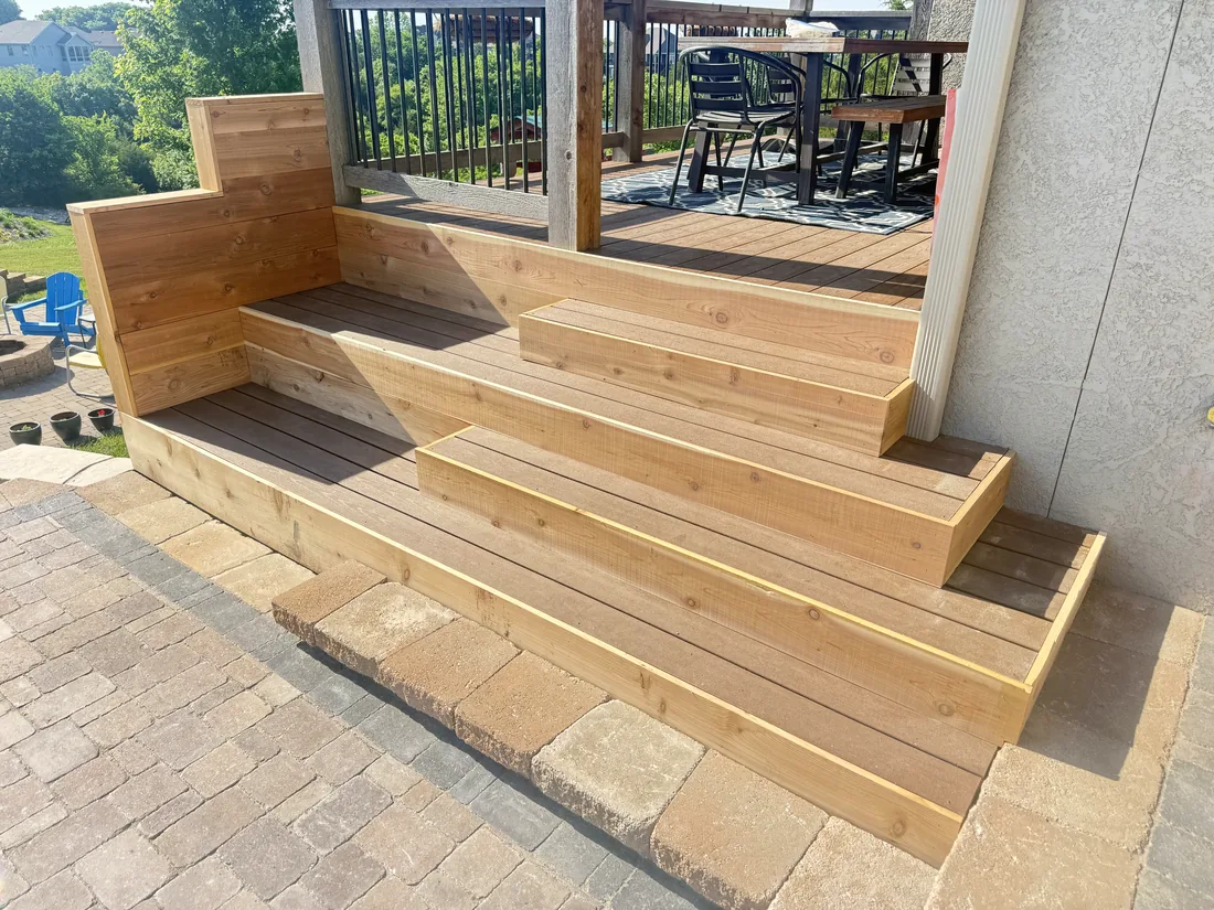 Wide cedar steps and a built in bench leading from a deck down to a paver patio