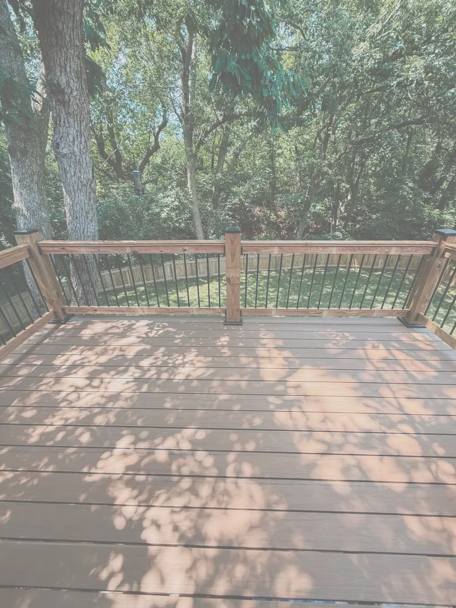 Composite deck boards and black metal railing on a wooded lot
