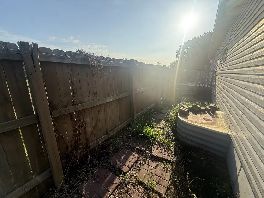 Broken and leaning fence boards at the corner of a yard before replacement