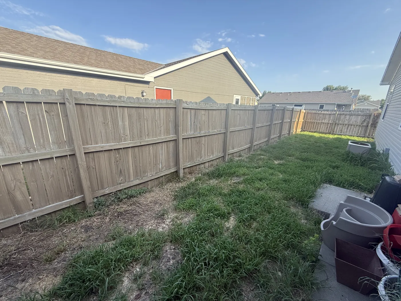 Leaning grey timber fence with gaps and weeds along a back yard before replacement