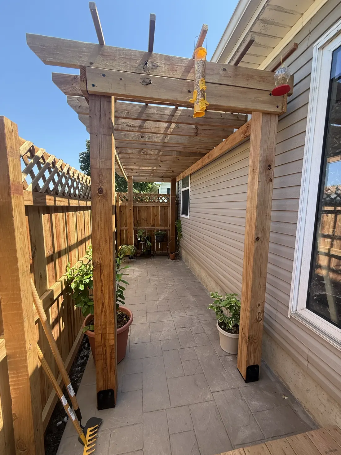 Cedar pergola beams and posts against a stone clad wall