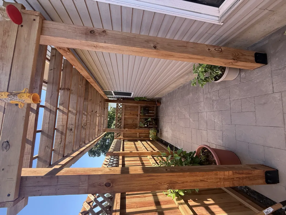 Cedar pergola frame carried on posts beside a stone wall