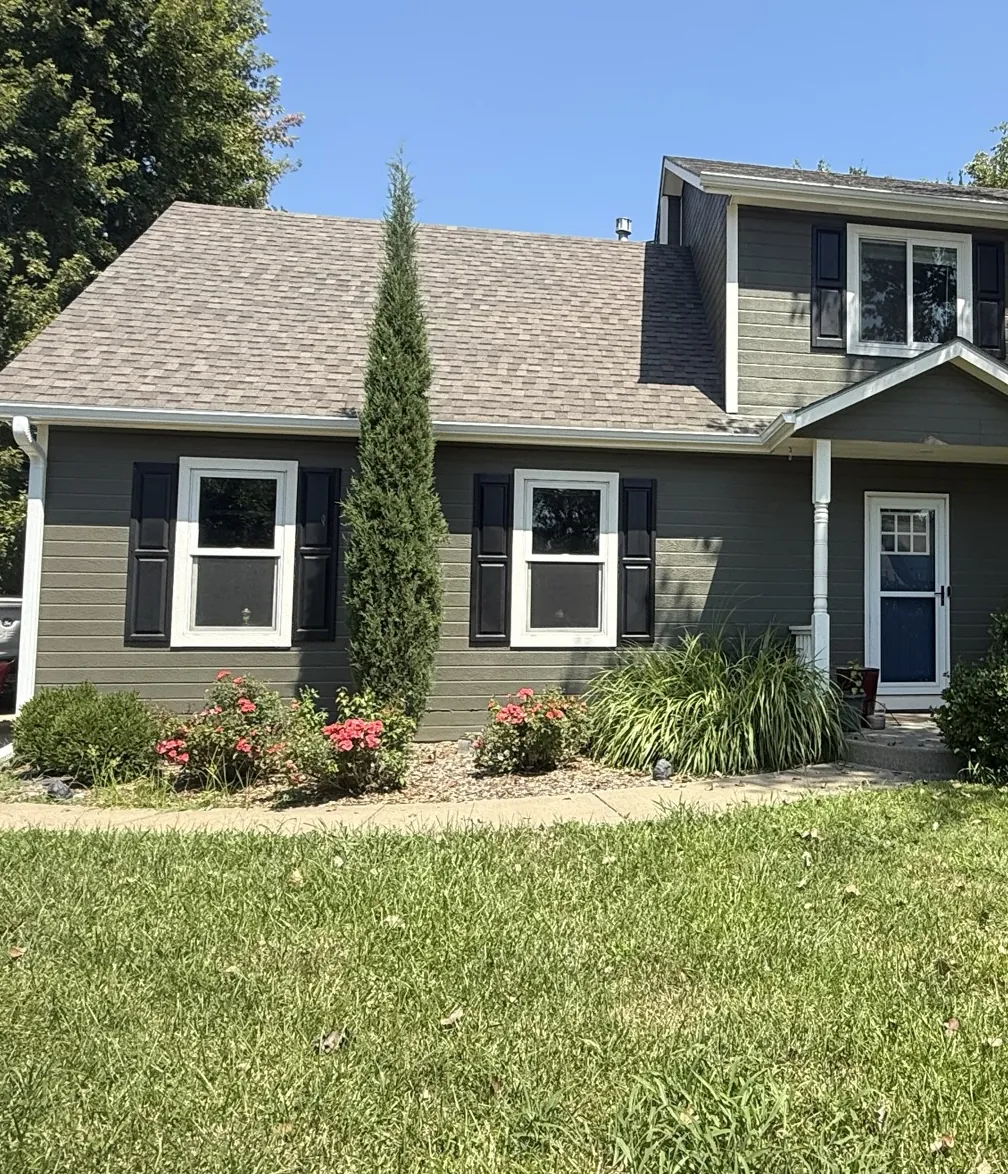 The same corner of the home after recladding in sage lap siding with black shutters