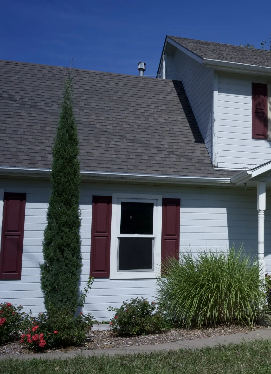 Two storey home in weathered white siding with maroon shutters before the recladding