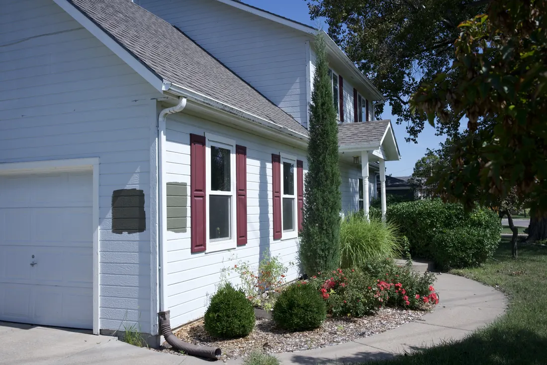 Side elevation of a white clad two storey home with red shutters
