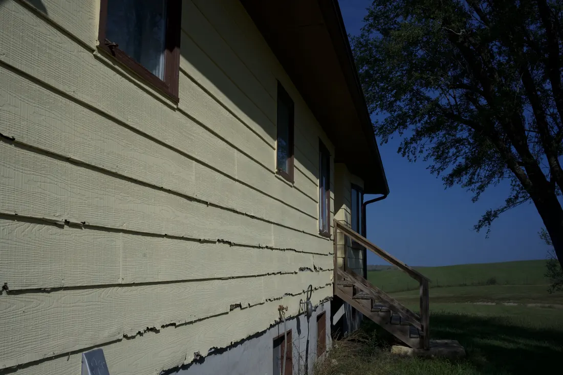 Close view of split and lifting siding boards on a yellow clad home