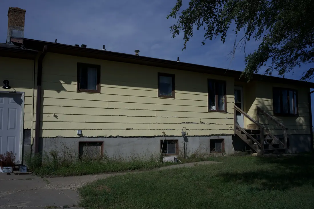 Long elevation of a yellow clad home showing cracked and lifting siding