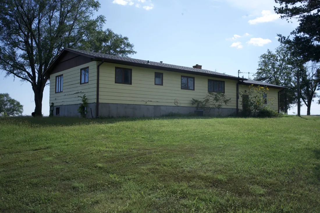 Yellow clad ranch home seen across the yard before the siding replacement